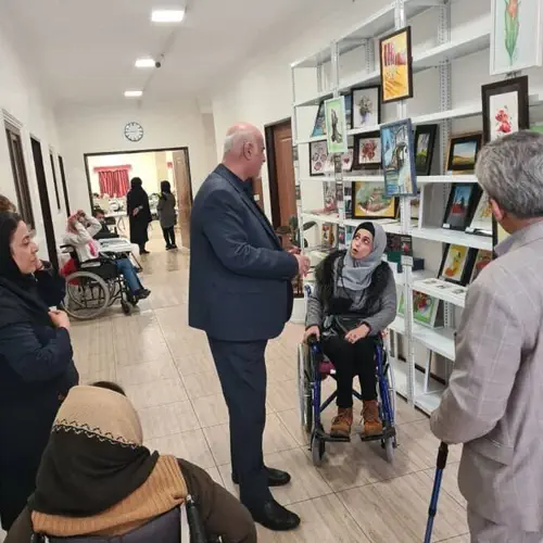 هنرمند دارای معلولیت در حال نمایش آثار نقاشی خود در غرفه بازارچه خیریه